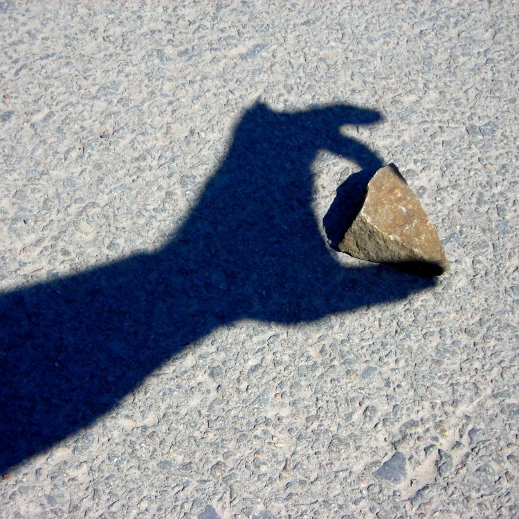 Schaduw van een hand grijpt naar een steen op de grond