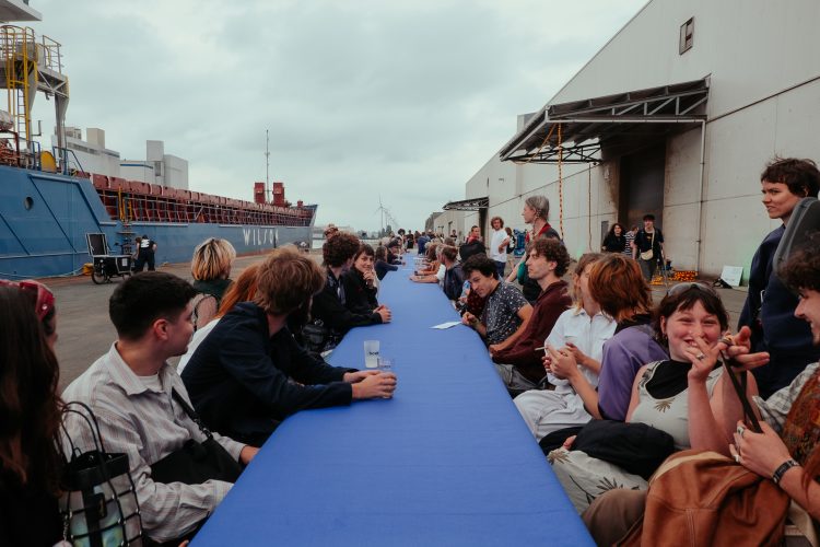 Een lange tafel opgesteld in de haven van Brugge waaraan een 50-tal mensen zitten, tijdens festival Konvooi